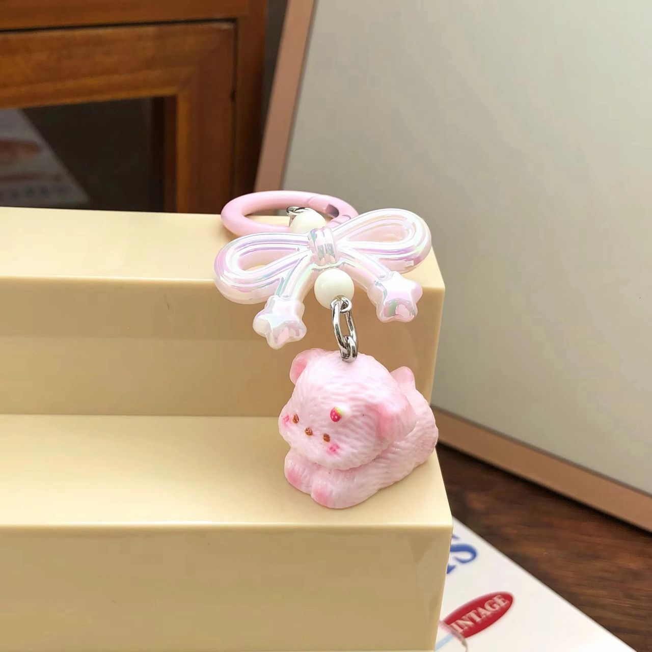 Pastel pink aesthetic keychain featuring an iridescent ribbon bow and a cute pink puppy figurine resting underneath.