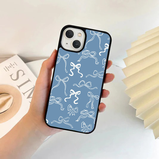 Hand holding a phone with a dusty blue case featuring a white sketched ribbon bow pattern.