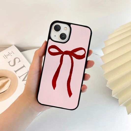 Hand holding a phone with a light pink case featuring a single large, textured red ribbon bow in the center.