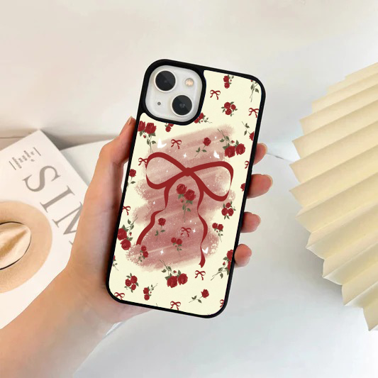 Cream-colored phone case with a large central red bow, scattered red roses, and delicate white sparkle accents.