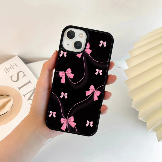 Black phone case decorated with bright pink ribbon bows connected by thin, winding pink strings.
