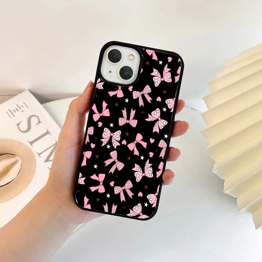 Black phone case featuring pink bows with a white daisy pattern inside, surrounded by tiny pink hearts and stars.