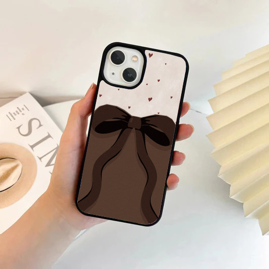 Phone case split horizontally; the top is cream with tiny red hearts, and the bottom features a large, dark brown flowing bow over a solid brown background.