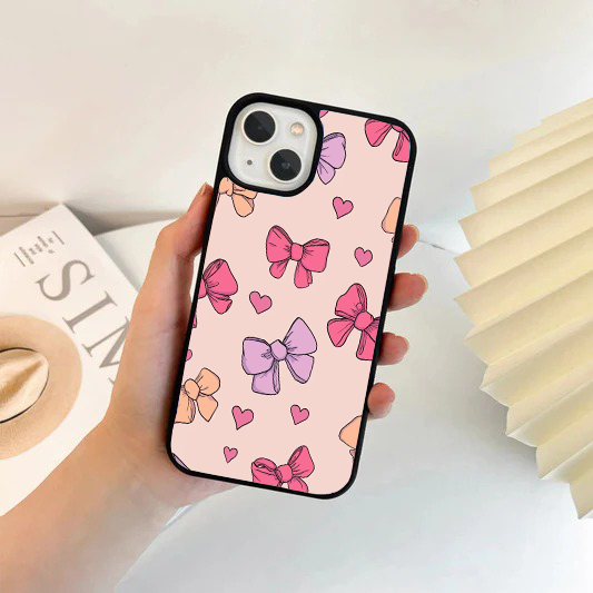 Soft pink phone case featuring a scattered pattern of pastel pink, purple, and peach bows along with tiny pink hearts.