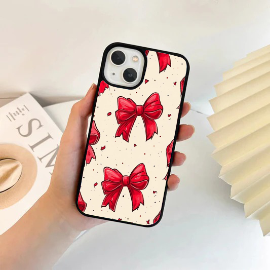 Cream-colored phone case decorated with large, detailed red ribbon bows and small red confetti speckles.