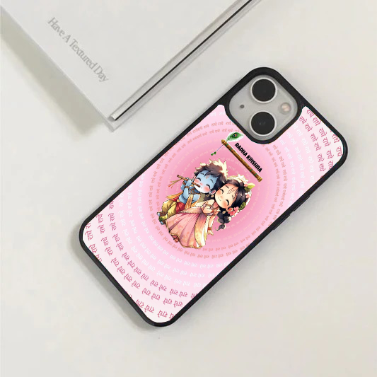 Pink phone case with a chibi anime illustration of Radha and Krishna playing the flute, surrounded by a circular text pattern of "Radhe Radhe".
