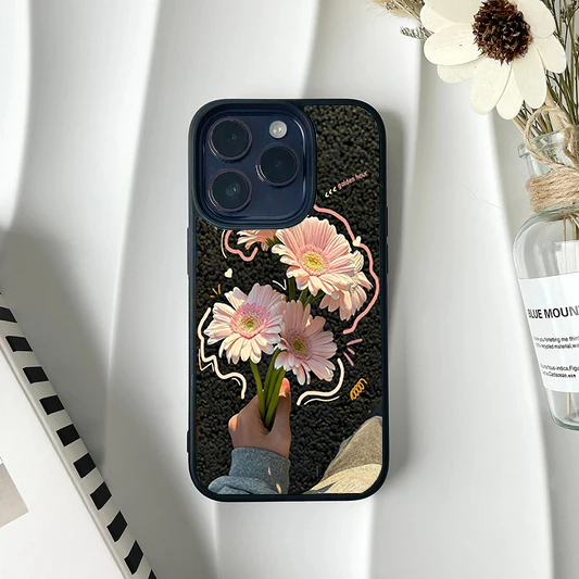 Phone case featuring a photo of a hand holding pink gerbera daisies against a dark background with cute doodle accents.