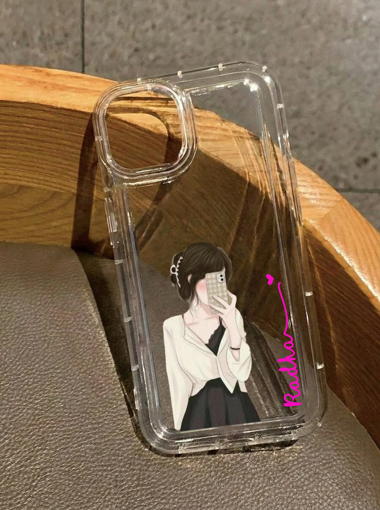 Clear iPhone 16 case featuring an illustration of a brunette girl in a white cardigan taking a mirror selfie, customized with the name Radha in pink handwriting.