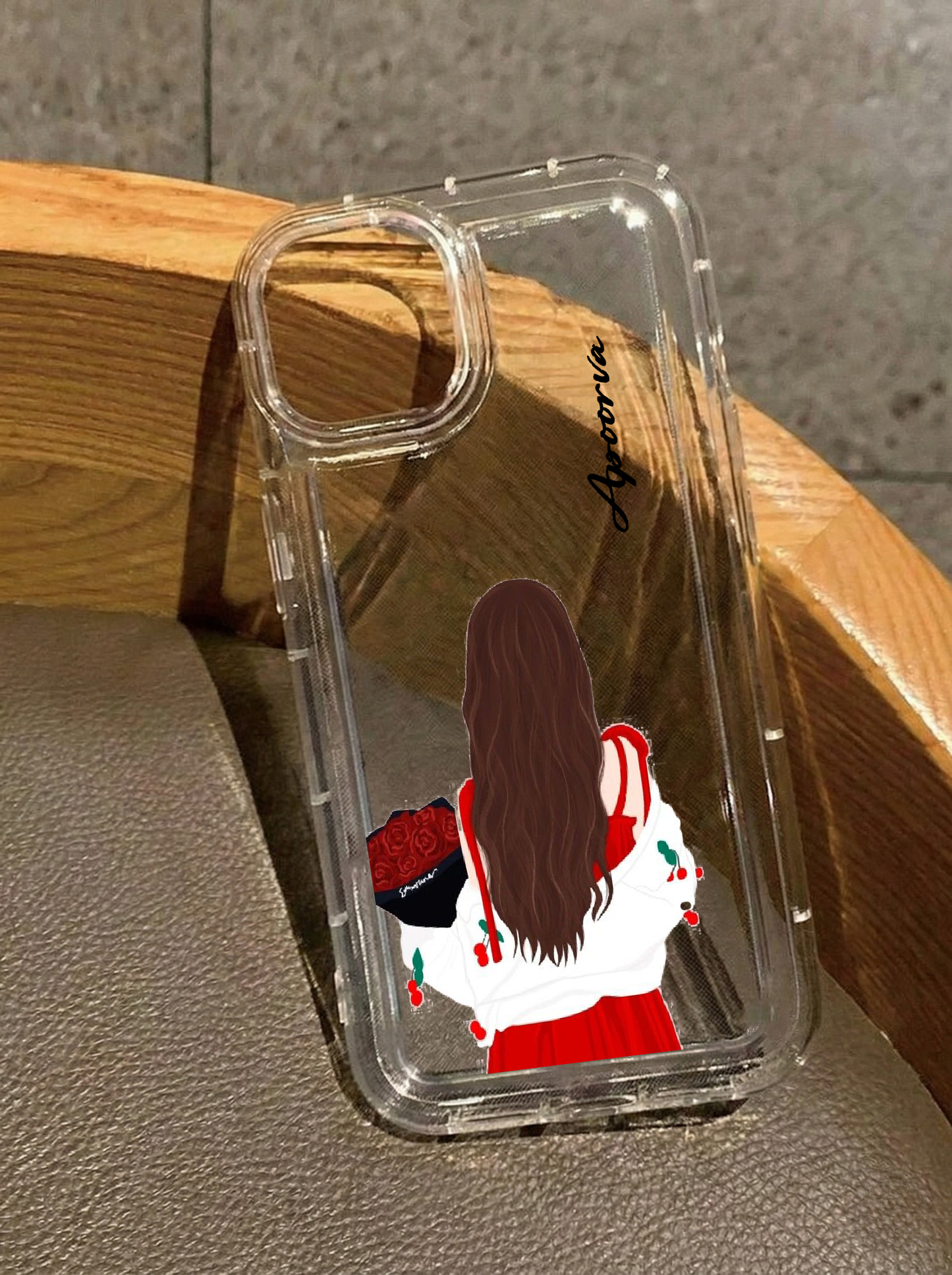 Clear iPhone 16 case displaying an illustration from behind of a girl in a red dress and white cherry cardigan holding a bouquet of red roses, personalized with the name Apoorva in vertical black text.